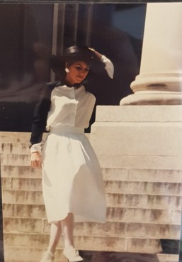 Student in black and white dress holding her hat in the wind.